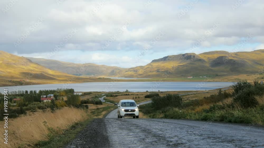 car with tourists is moving over road between beautiful mountains in Iceland in fall day