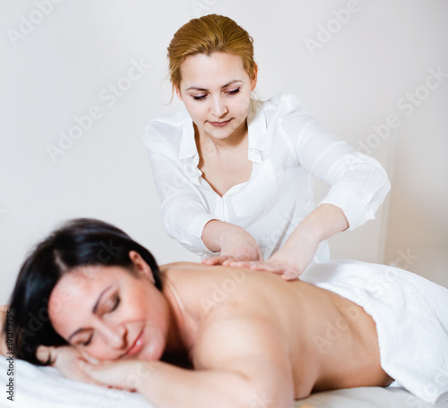 Young massagist doing shoulder massage to adult woman