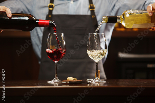 Canvas Print Male sommelier pouring red and white wine into long-stemmed wineglasses