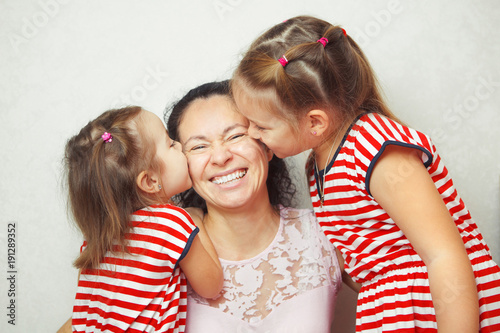 Two little daughters kiss their mother in cheeks