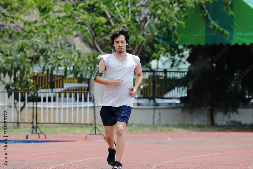 Handsome athlete Asian man running on racetrack in stadium with copy space background. Healthy active lifestyle concept. Handsome athlete Asian man running on racetrack in stadium with copy space background. Healthy active lifestyle concept.
