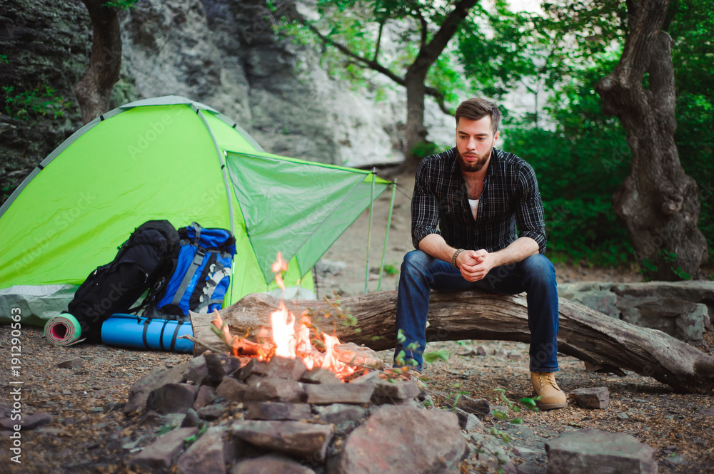 Traveler man relaxing, looking at the fire and dreaming at camping tent outdoors on nature. Traveler man relaxing, looking at the fire and dreaming at camping tent outdoors on nature.