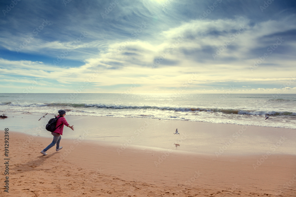 A girl traveler runs after seagulls on the ocean, a beautiful seascape. Portugal, Algarve