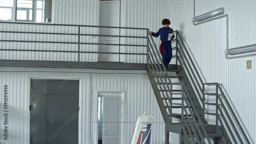 Female aircraft maintenance supervisor entering hangar and going downstairs to light jet airplane Female aircraft maintenance supervisor entering hangar and going downstairs to light jet airplane