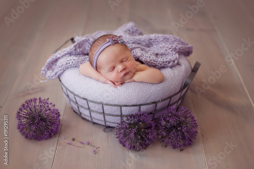 newborn baby sleeping in a basket, on a wooden background and purple onions