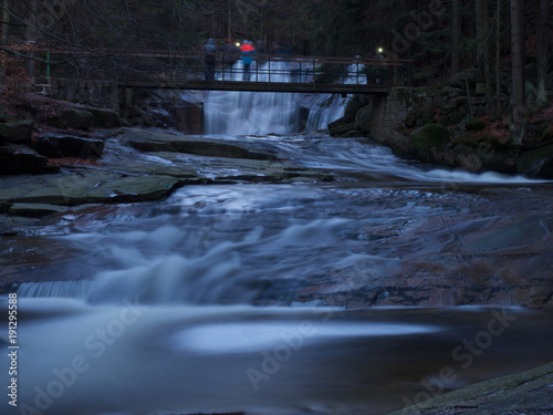 Fluss mit Wasserfall und Brücke am Abend mit Personen