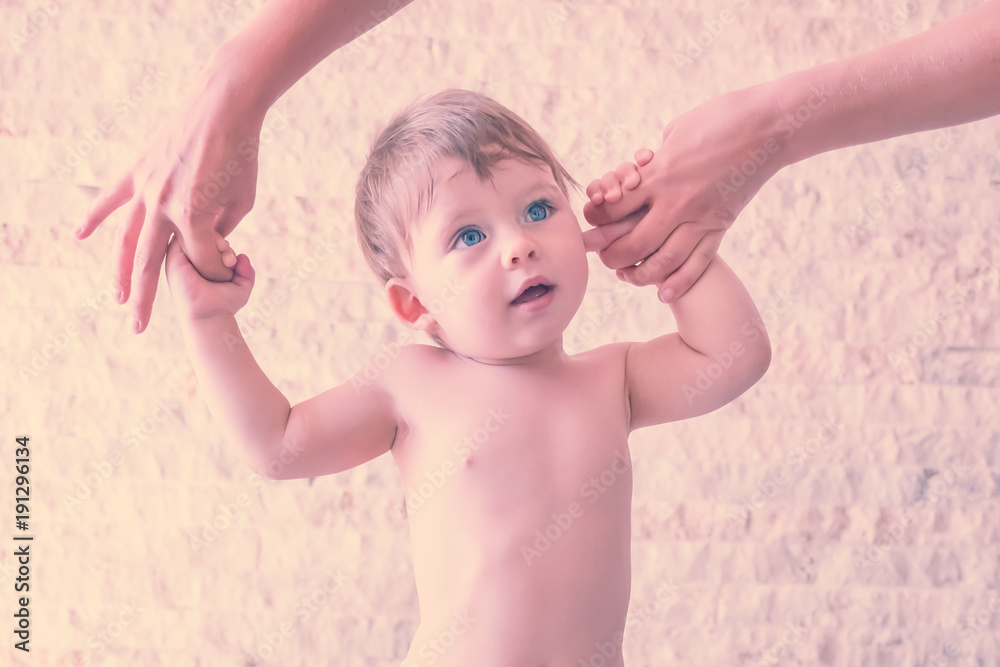 Fototapeta premium Cute blue-eyed baby boy making the first steps with the help of the mother. Toned
