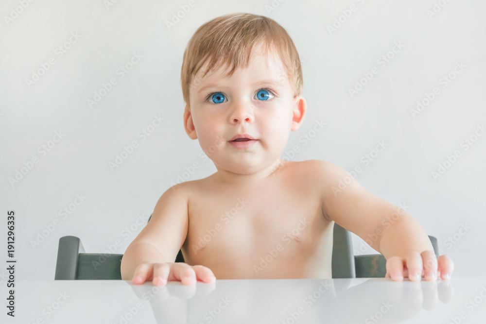 Portrait of a blonde baby boy with blue eyes sitting at the table Portrait of a blonde baby boy with blue eyes sitting at the table