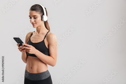 Portrait of caucasian pretty woman listening to music using wireless headphones in studio after workout, isolated over gray background