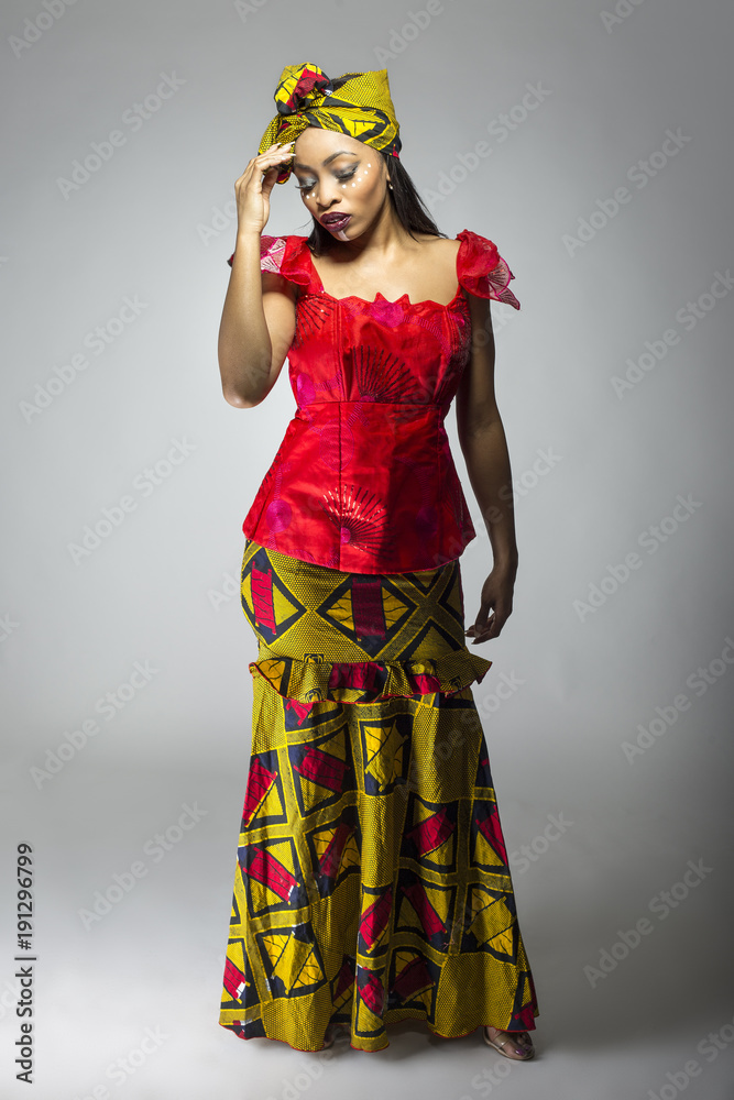 Black female showing african pride by wearing a traditional Nigerian dress  and head scarf with tribal face markings or cosmetic makeup. The costume is  red and yellow and shows cultural fashion. Photos