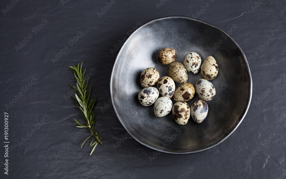 Quail eggs in ceramic black bowl on black ceramic background and green rosemary Quail eggs in ceramic black bowl on black ceramic background and green rosemary