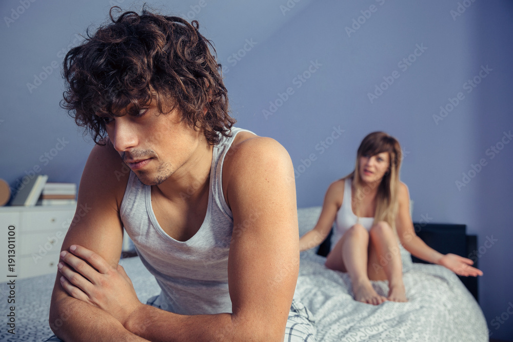 Portrait of thoughtful man sitting over bed and listening to angry woman having argument in a quarrel. Couple relationship and problems concept. Portrait of thoughtful man sitting over bed and listening to angry woman having argument in a quarrel. Couple relationship and problems concept.