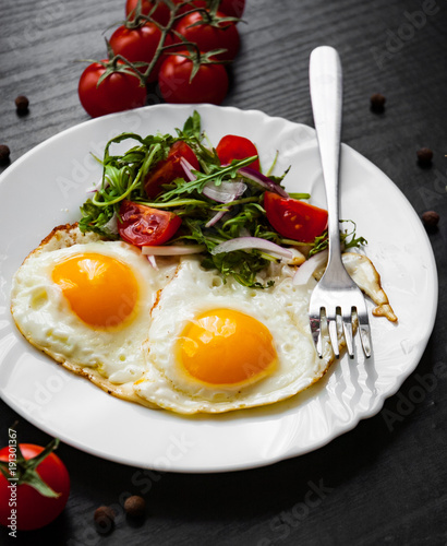 Breakfast. Fresh salad and two fried eggs on dark wooden background