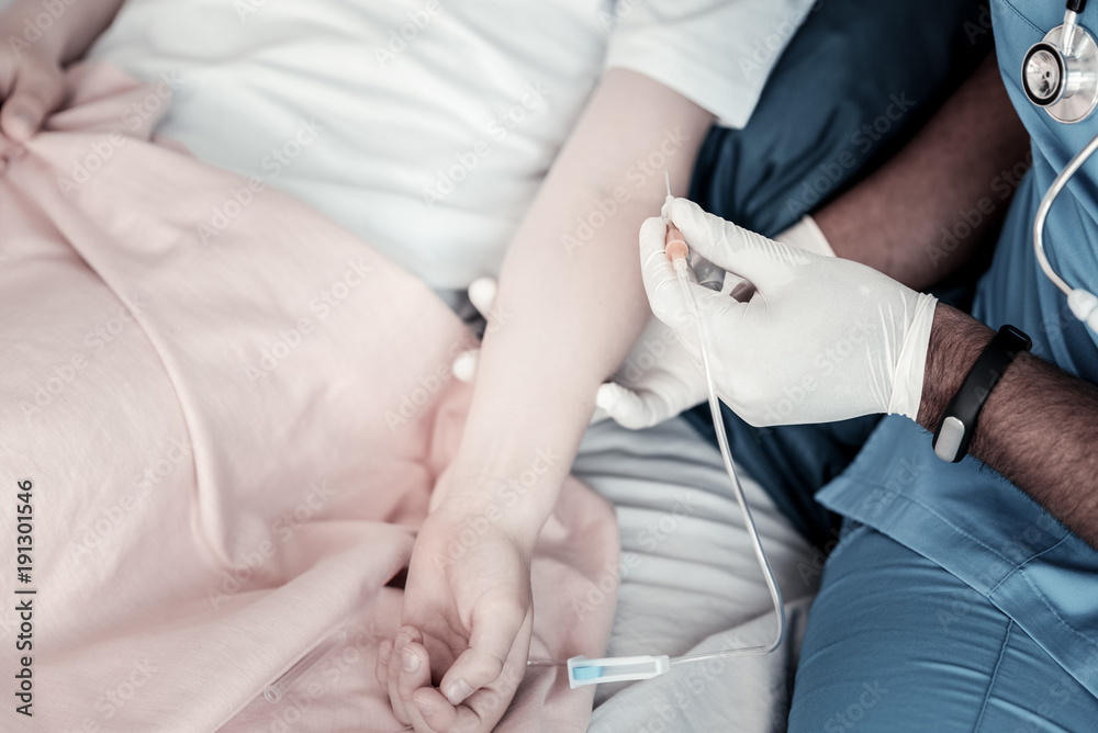This will not hurt you. Close up a male medical worker wearing gloves getting ready to put a drip on an arm of his patient at hospital. This will not hurt you. Close up a male medical worker wearing gloves getting ready to put a drip on an arm of his patient at hospital.