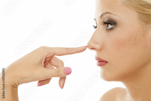 Young blonde touches her nose on white background