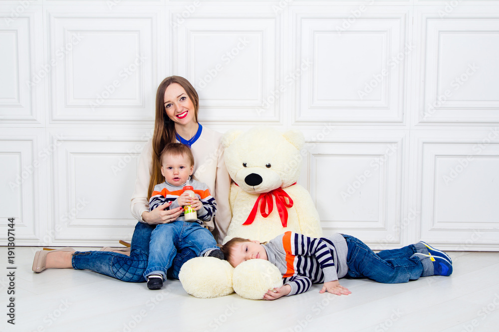 young mother with two children and Teddy bear. family happiness, mom and two sons in jeans sitting on the floor young mother with two children and Teddy bear. family happiness, mom and two sons in jeans sitting on the floor