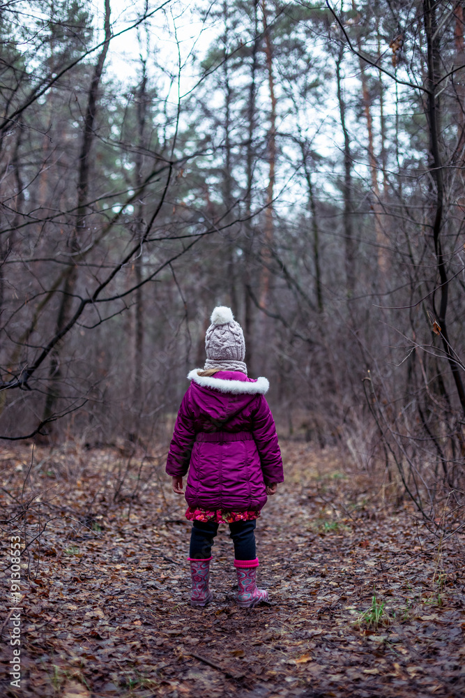A little girl is standing in a forest on a path. A little girl is standing in a forest on a path.