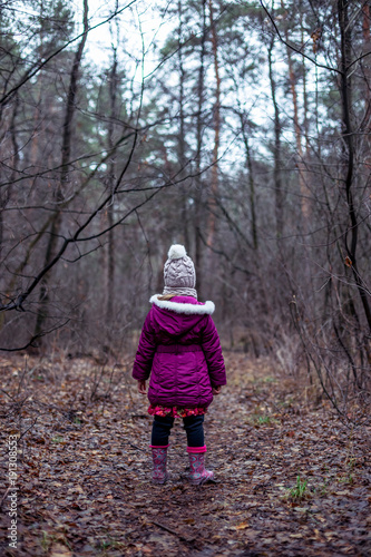 A little girl is standing in a forest on a path.