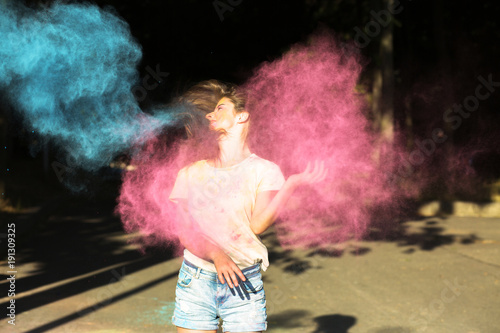 Pretty brunette woman with wind in hair playing with blue and pink dry paint Holi