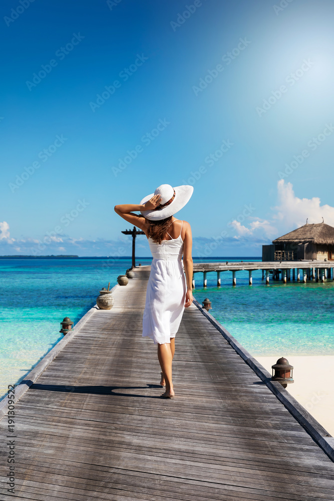 Elegante Touristin in weiß läuft auf einem Holzsteg auf den Malediven