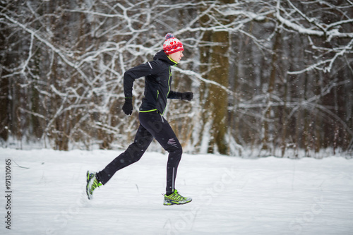 Image from side of man in sportswear, red cap on run in winter