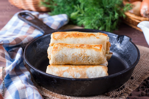 Crepes stuffed with minced meat and rice in a frying pan on a wooden table