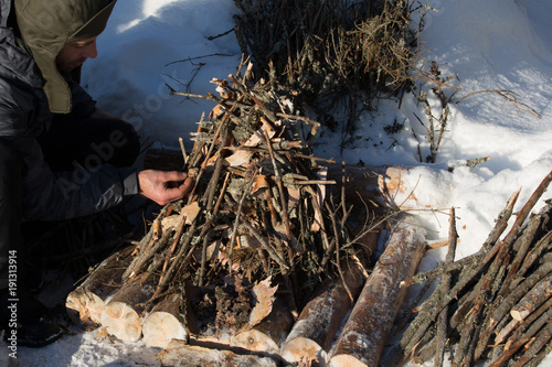 Campfire in deep snow, preparation, wooden pyramid of small and medium-sized wood and birch bark, man distributed tree resin photo