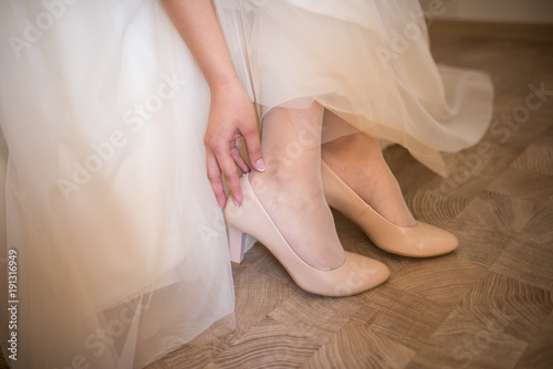 The bride touches her beige wedding shoes. The bride is wearing her wedding shoes. Wedding day. 