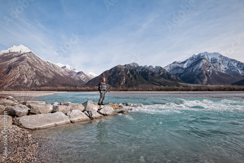 Man hiker on shore of river looking the mountains.