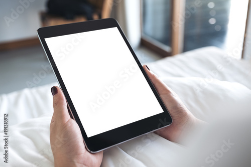 Mockup image of woman's hands holding black tablet pc with blank desktop white screen while sitting on a white bed
