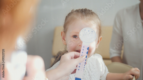 Cute blonde girl with mommy in child's ophthalmology - optometrist diagnosis eyesight photo