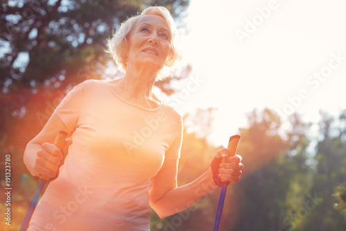 Bright day. Close up of elderly woman having splendid mood while walking with a help of crutches