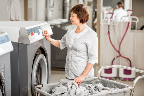 Slika na platnu Senior washwoman in uniform working with washing machine in the professional hot
