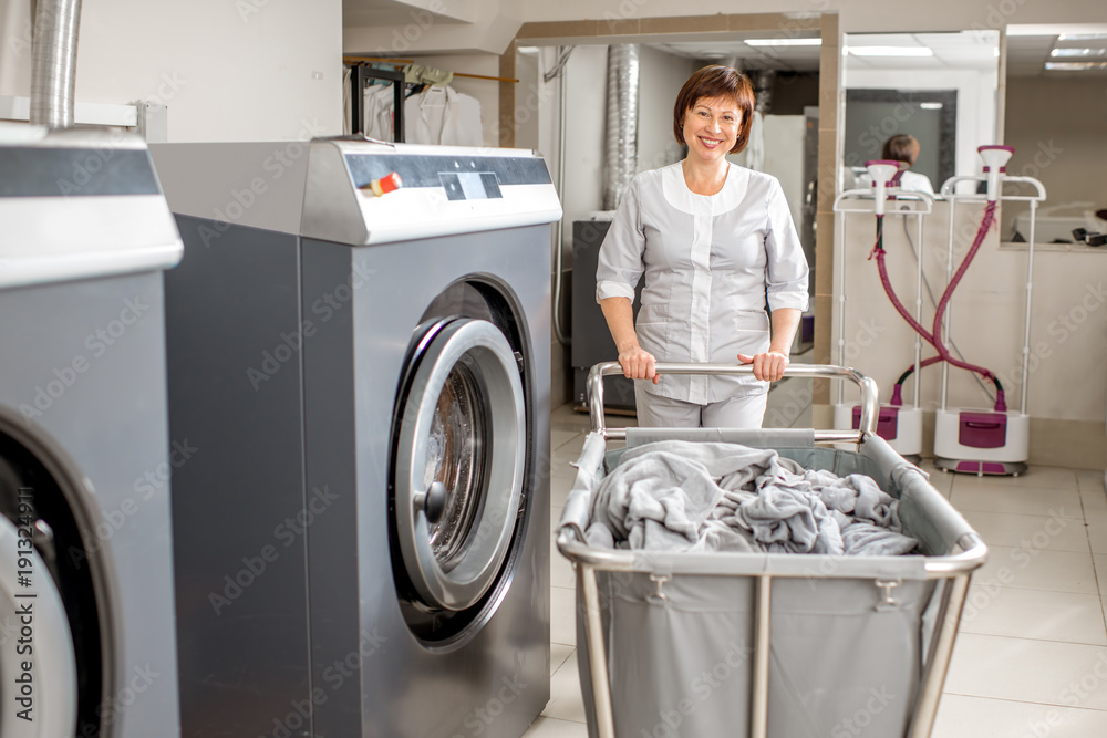 Senior washwoman in uniform standing with clothes basket near the wahing  machine in the professional hotel laundry Stock Photo | Adobe Stock