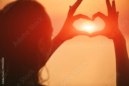 silhouette of a beautiful sexual girl against the sea and sunset. happy woman enjoying summer vacation. Woman shows a heart by hands