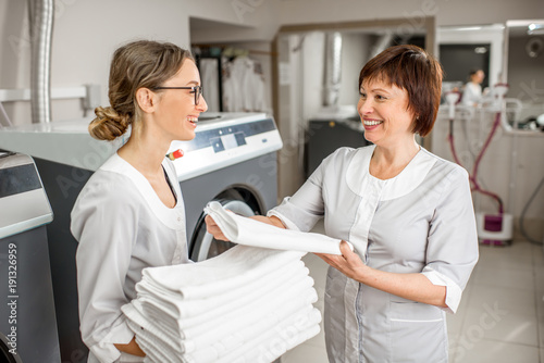 Принти на полотні Senior washwoman making up clean towels with young assistant in the hotel laundr