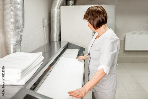 Senior woman in unifrom working with professional ironing machine in the laundry