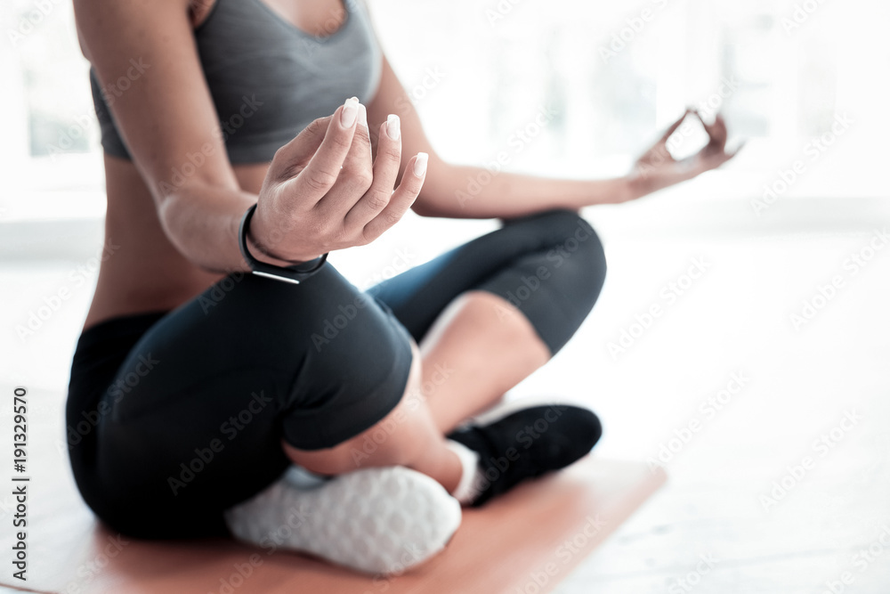 Getting my thoughts all together. Selective focus on a hand of a young lady sitting in a half lotus position and getting relaxed while practicing yoga.