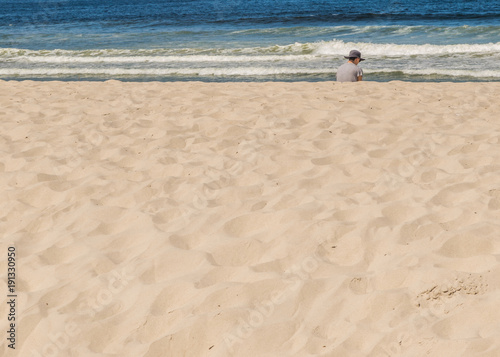 Man in a sunhat sitting on a beach