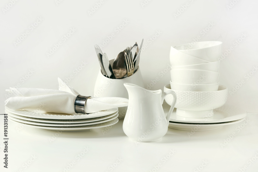White tableware for serving. Crockery,dish, utensils and other different white stuff on white table-top. Kitchen still life as background. Copy space. White tableware for serving. Crockery,dish, utensils and other different white stuff on white table-top. Kitchen still life as background. Copy space.