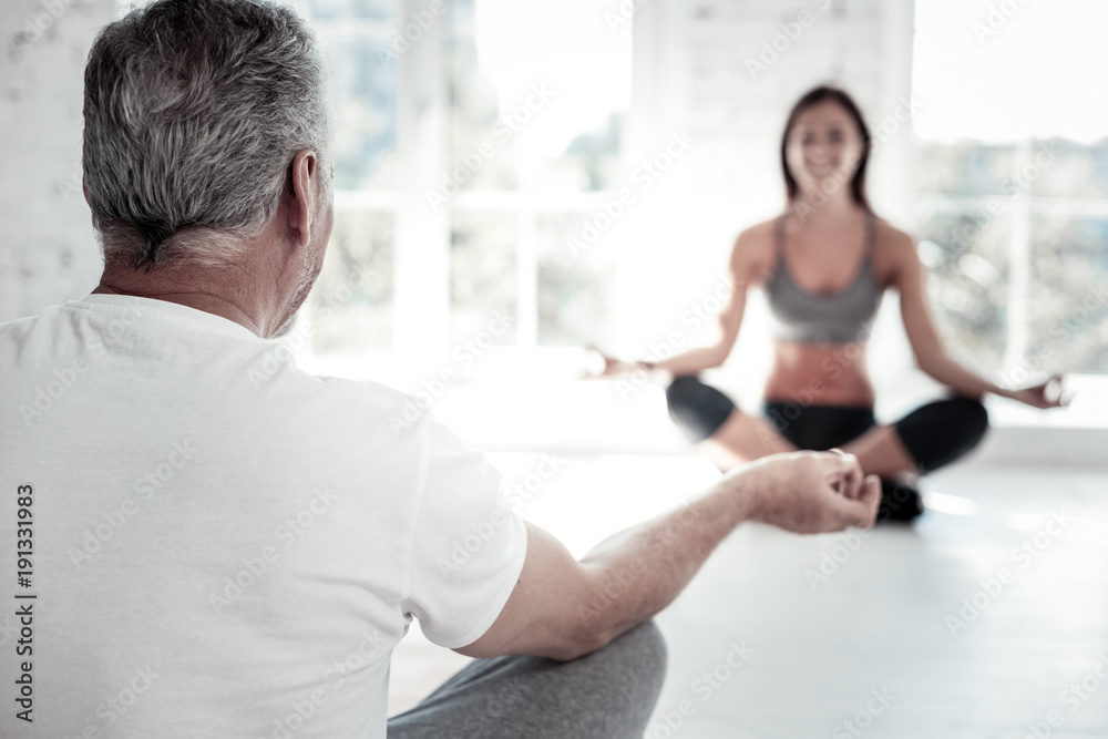 Getting relaxed. Turned back senior man sitting in a lotus position and meditating while attending a yoga class indoors. Getting relaxed. Turned back senior man sitting in a lotus position and meditating while attending a yoga class indoors.