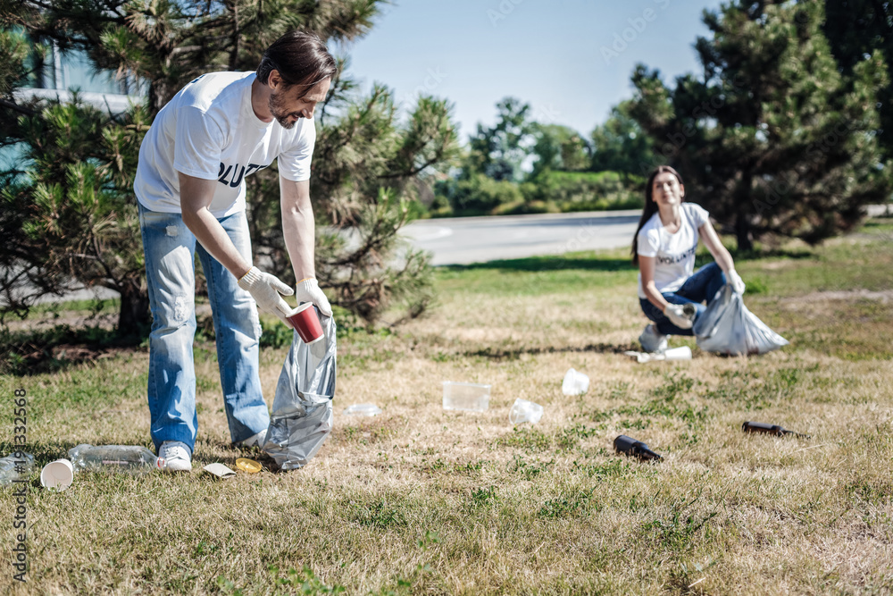 Eco project. Happy positive nice man holding a plastic bag and cleaning rubbish while participating in eco project Eco project. Happy positive nice man holding a plastic bag and cleaning rubbish while participating in eco project