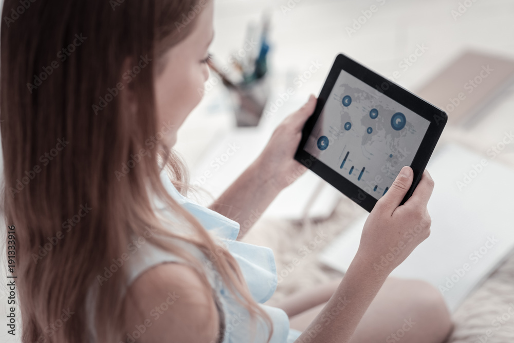 Finding information. Long-haired girl holding a black tablet and looking at the screen while wearing a blue shirt