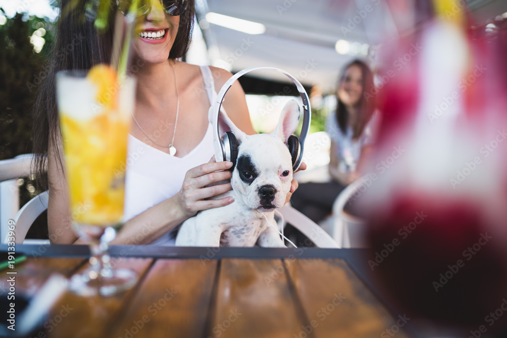 Beautiful young woman with sunglasses sitting in cafe with her adorable French bulldog puppy. People with dogs theme.