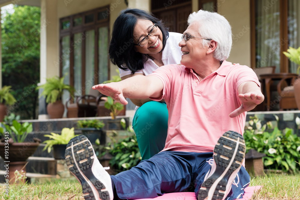 Cheerful senior woman helping her partner during workout session outdoors in the yard