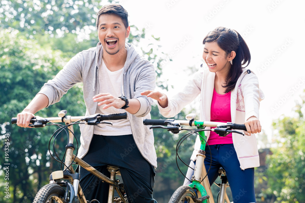 Obraz premium Young Asian couple laughing together while riding bicycles outdoors in summer 