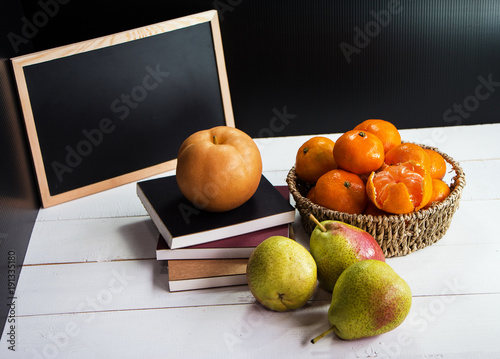 The Chinese pear put on stacked books and group of orange put in woven basket, beside three pears on wooden timber board,they are put in front of chalk board, photo