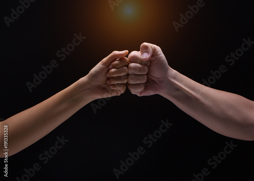 Close up of human hands making a fist bump on black background.  a fist pump together after good deal. Business success and teamwork concept.blurry light around.