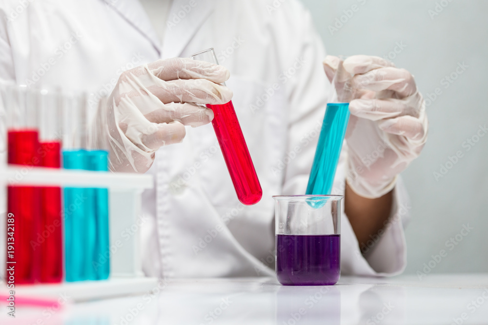 Hand of a chemist  showing red and blue liquid chemicals in tubes and eggplan liquide chemicals in beaker