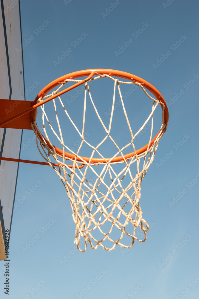 Closeup basketball hoop, basket with white net and blue sky in background